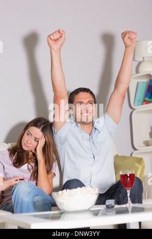 Aufgeregt Mann vor dem Fernseher mit Wein und Popcorn von gelangweilten Frau zu Hause Stockfoto
