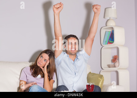 Aufgeregt Mann vor dem Fernseher mit Wein von einer gelangweilten Frau zu Hause Stockfoto