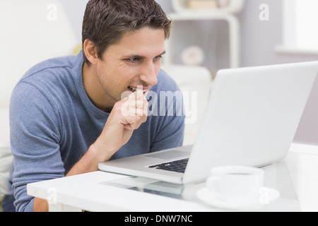 Nachdenklicher junger Mann mit Laptop im Wohnzimmer Stockfoto