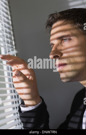 Ernst junger Geschäftsmann spähen durch Jalousien im Büro Stockfoto