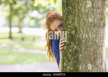 Niedliche Rothaarige versteckt sich hinter einem Baum Stockfoto