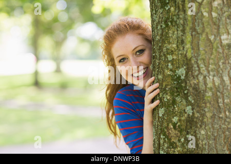 Lächelnde Rothaarige versteckt sich hinter einem Baum Stockfoto