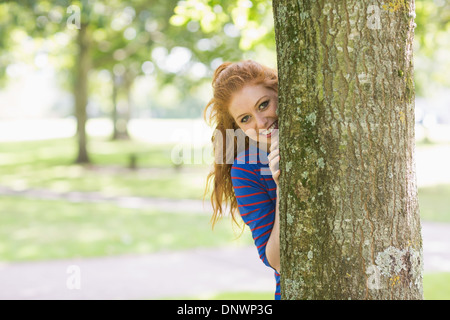 Lächelnde hübsche Rothaarige versteckt sich hinter einem Baum Stockfoto