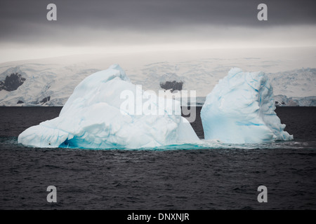 Antarktis - ein Eisberg schwebt in der eiskalten Wasser des Curtis Bay auf der Antarktischen Halbinsel. Während zwei getrennte Abschnitte über dem Wasser erscheinen, die Abschnitte werden durch eine viel größere mit einem Abschnitt unter dem Wasser verbunden.