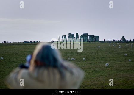 Eine Frau mit langen Haaren Blick auf Stonehenge durch ein Fernglas bei Sonnenuntergang von der Allee, Wiltshire, England Stockfoto