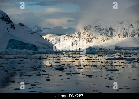 Antarktis - Die untergehende Sonne wirft einen schönen orange Glühen auf Wolken und Berge der dramatischen Landschaft von Paradise Harbour in der Antarktis, Antarktis. Stockfoto