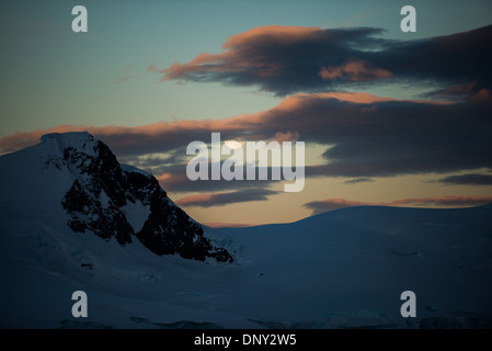 Antarktis - der Mond erhebt sich über einem dramatischen schneebedeckten Berg im Paradise Harbour Antarktis während die untergehende Sonne ein goldenes Leuchten auf den Wolken Fänge. Stockfoto