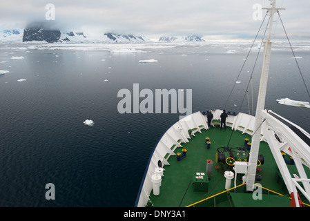 Lemaire-Kanal-Expeditionsschiff-Bug Antarktische Halbinsel | LEMAIRE-KANAL, Antarktis — Der Bug eines Expeditionsschiffs nähert sich dem nordöstlichen Eingang des Lemaire-Kanals, sein grünes Vordeck und die Ankerausrüstung werden von verstreutem Scholleneis eingerahmt. Der Kanal wurde von Adrien de Gerlache nach seinem Freund Charles Lemaire, einem Offizier des Belgischen Kongo-Freistaats, benannt und erstreckt sich etwa 7 Meilen (11 km) zwischen Booth Island und der Graham-Küste und kann bei starkem Eis vollständig abschließen. Stockfoto