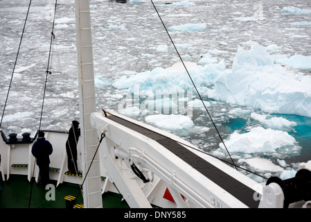 Antarktis - Fahrgäste stehen auf dem Bug eines ice-gestärkt Kreuzfahrtschiff, wie es navigiert der Lemaire Kanal mit der Oberfläche des Wassers mit Glatteis und brash Eis bedeckt. Die Lemaire Kanal wird manchmal auch als "Kodak Lücke' in einem Kopfnicken zu seiner berühmt malerische Aussicht bezeichnet. Stockfoto