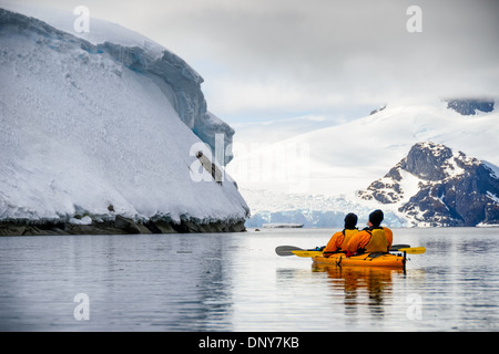 Kayakers Petermann Island Antarktis | PETERMANN ISLAND, Antarktis – zwei Kajakfahrer paddeln in einem Tandem-Kajak unter eisbedeckten Klippen in der Nähe von Petermann Island, im Wilhelm-Archipel südlich des Lemaire-Kanals. Die Insel beherbergt Brutkolonien von Gentoo- und Adélie-Pinguinen in der Nähe der Rande ihrer Gebirgszüge, was sie zu einem häufigen Ort für Forschungsreisen und Expeditionen auf der westlichen Antarktischen Halbinsel macht. Stockfoto