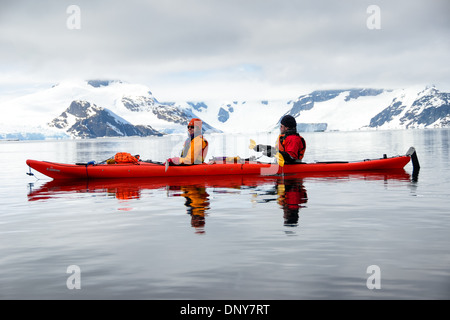 Kajakfahrer in einem Tandem-Kajak gleiten über glasige Stillgewässer auf Petermann Island auf der antarktischen Halbinsel. Stockfoto