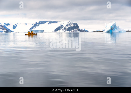 Kajakfahrer in einem Tandem-Kajak gleiten über glasige Stillgewässer auf Petermann Island auf der antarktischen Halbinsel. Stockfoto