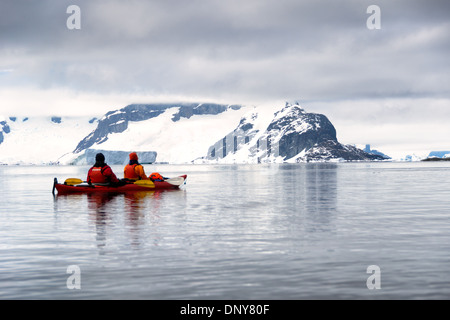 Kajakfahrer in einem Tandem-Kajak gleiten über glasige Stillgewässer auf Petermann Island auf der antarktischen Halbinsel. Stockfoto