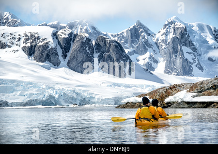 Antarktis - Kayaker paddeln entlang der glasigen Bedingungen neben malerischen Bergen an der Küste in der Nähe von Petermann Island an der Westküste der Antarktischen Halbinsel. Stockfoto