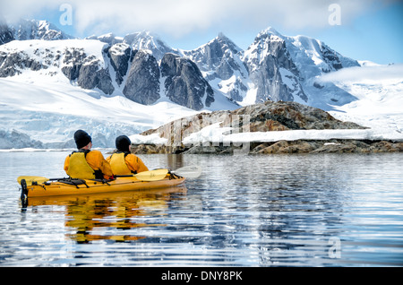 Antarktis - Kayaker paddeln entlang der glasigen Bedingungen neben malerischen Bergen an der Küste in der Nähe von Petermann Island an der Westküste der Antarktischen Halbinsel. Stockfoto