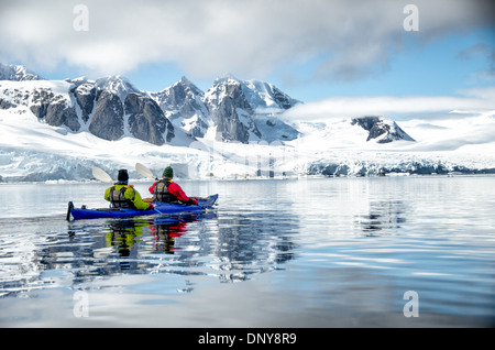 Antarktis - Kayaker paddeln entlang der glasigen Bedingungen neben malerischen Bergen an der Küste in der Nähe von Petermann Island an der Westküste der Antarktischen Halbinsel. Stockfoto