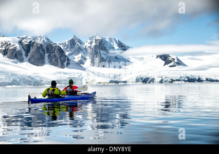 Antarktis - Kayaker paddeln entlang der glasigen Bedingungen neben malerischen Bergen an der Küste in der Nähe von Petermann Island an der Westküste der Antarktischen Halbinsel. Stockfoto