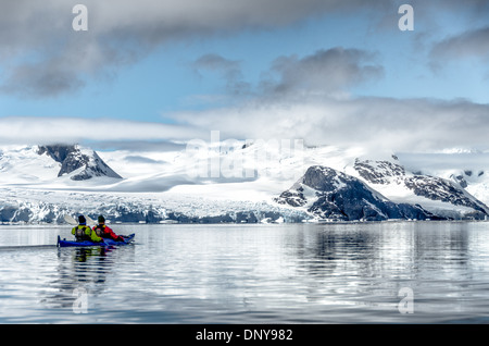 Antarktis - Kayaker paddeln entlang der glasigen Bedingungen neben malerischen Bergen an der Küste in der Nähe von Petermann Island an der Westküste der Antarktischen Halbinsel. Stockfoto