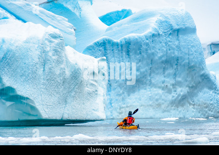 Antarktis - ein solo Kayaker navigiert durch eine Öffnung zwischen großen blauen Eisberge in einem Eisberg Friedhof in einer Bucht bei Melchior Island auf der Antarktischen Halbinsel. Stockfoto