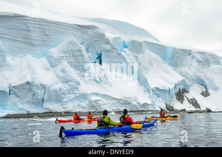 Antarktis - Kayaker paddeln an massiven Klippen von Gletschereis langsam Einschieben in die See entlang der Uferpromenade am Melchior Insel an der Westküste der Antarktischen Halbinsel. Stockfoto