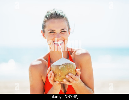 Glückliche junge Frau trinken Kokosmilch am Strand Stockfoto