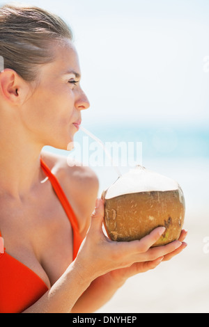 Porträt der glückliche junge Frau trinken Kokosmilch am Strand Stockfoto