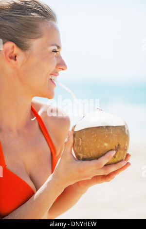 Glückliche junge Frau trinken Kokosmilch am Strand Stockfoto