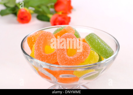 Bunte Bonbons mit zwei roten Herzen in Glasschale und Rosen, Nahaufnahme Stockfoto