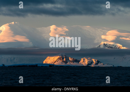 Berge der Antarktischen Halbinsel Sonnenuntergang Hughes Bay / HUGHES BAY, Antarktis — Alpenglow fängt die Gletscherspitzen oberhalb der Hughes Bay auf der westlichen Antarktischen Halbinsel um Mittsommer Mitternacht, wenn die Sonne in diesem Breitengrad kaum unter den Horizont fällt. Die Antarktische Halbinsel liegt im Dezember in der Dämmerungszone des Polarkreises und bietet Expeditionsschiffen täglich ein fast 20-stündiges Zeitfenster mit nutzbarem Licht. Stockfoto