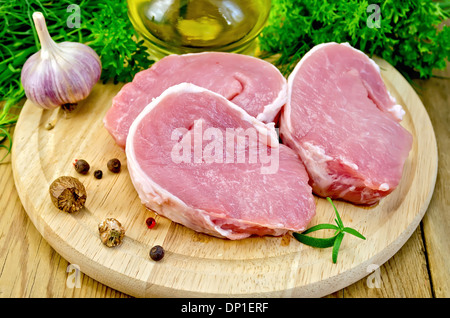 Drei Stück von Schweinefleisch, Knoblauch, Muskatnuss, Petersilie, Öl, Rosmarin und Dill, Paprika, auf einem runden Holzbrett Stockfoto