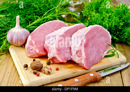 Drei Stück von Schweinefleisch, Knoblauch, Muskatnuss, Petersilie, Estragon, Rosmarin und Dill, Messer, Pfeffer auf einem Holzbrett Stockfoto