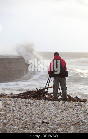 Ein Fotograf macht Fotos von Winterwellen, die über die Maiskolben in Lyme Regis. Stockfoto