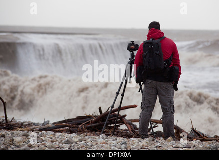 Ein Fotograf macht Fotos von Winterwellen, die über die Maiskolben in Lyme Regis. Stockfoto