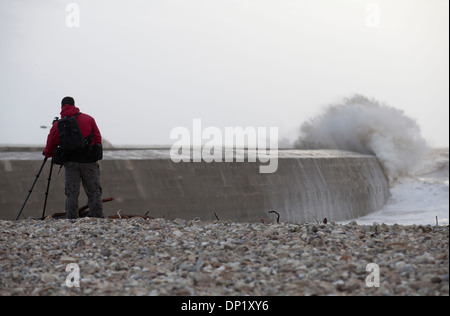 Ein Fotograf macht Fotos von Winterwellen, die über die Maiskolben in Lyme Regis. Stockfoto