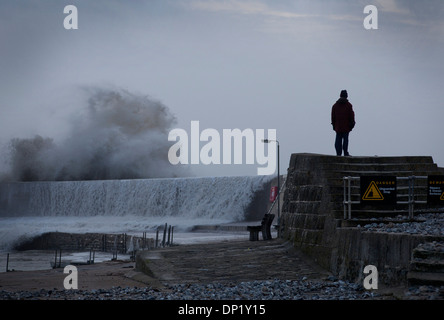 Ein Mann steht auf dem Kolben in Lyme Regis mit großen Wellen, die über und stürmischer See. Stockfoto