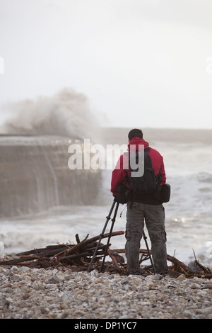 Ein Fotograf macht Fotos von Winterwellen, die über die Maiskolben in Lyme Regis. Stockfoto