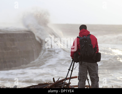 Ein Fotograf macht Fotos von Winterwellen, die über die Maiskolben in Lyme Regis. Stockfoto