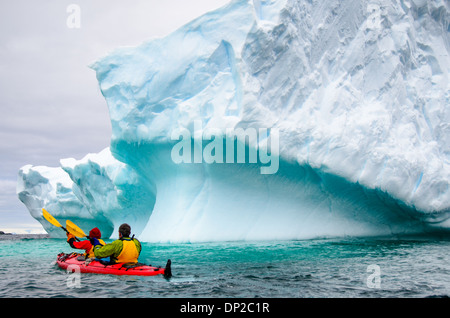 Antarktis - Kajakfahrer in einem Tandem kayak vorbei ein Eisberg, der langsam an Hydrurga Felsen an zwei hummock Insel kippen. Die Region ist bekannt als Favorit für die seeleoparden (Hydrurga leptonyx). Stockfoto