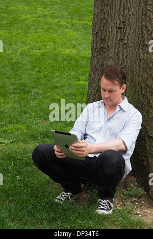 Ein Mann lehnt sich an einen Baum hält eine iPad 3g 64gb Stockfoto
