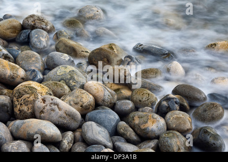 Kieselsteine am Strand mit dem Meer um sie herum Läppen Stockfoto