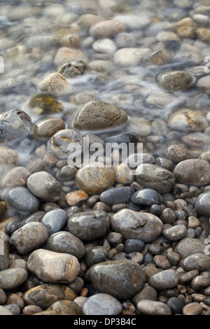 Kieselsteine am Strand mit dem Meer um sie herum Läppen Stockfoto