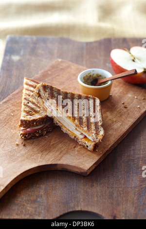 Gegrillter Käse Panini mit Cheddar und Apfel, eine halbe rote Apfel und Dijon-Senf in kleinen Schüssel auf Schneidebrett, Studioaufnahme Stockfoto