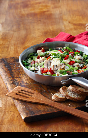 Pfanne mit Gemüse und Rührei zum Frühstück, mit ganzen Weizen getoastetes Baguette auf Schneidebrett, Studioaufnahme Stockfoto