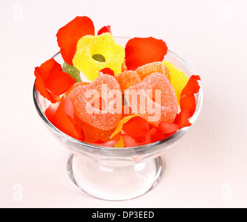 Zwei rote Herzen Bonbons in Glasschale und Rosenblüten, Nahaufnahme Stockfoto