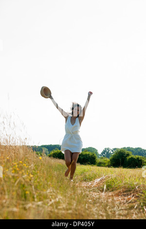 Teenager Mädchen mit Strohhut mit Armen in der Luft, zu Fuß im Feld an einem Sommertag, Deutschland Stockfoto