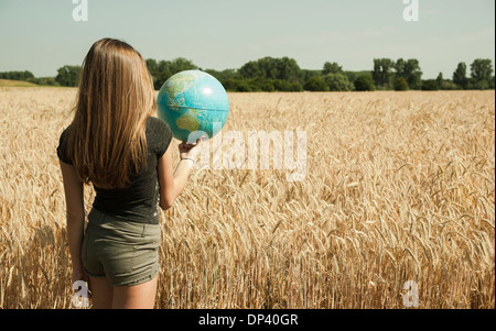 Rückansicht der Teenager Mädchen stehen im Weizenfeld, halten Globus, Deutschland Stockfoto