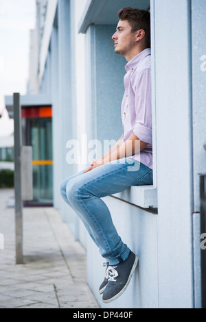 Junger Mann sitzt auf Felsvorsprung im Freien, Deutschland Stockfoto