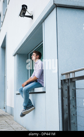 Junger Mann sitzt auf Felsvorsprung im Freien, Deutschland Stockfoto