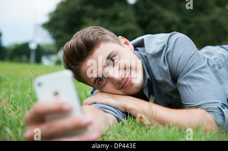 Nahaufnahme der junge Mann liegt auf dem Rasen, Blick auf Handy, Deutschland Stockfoto