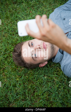 Erhöhte Ansicht der junge Mann liegt auf dem Rasen, Blick auf Handy, Deutschland Stockfoto